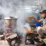 Un vendeur de rue grillant des brochettes de satay sur un marché traditionnel de Yogyakarta