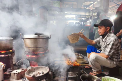 Un vendeur de rue grillant des brochettes de satay sur un marché traditionnel de Yogyakarta