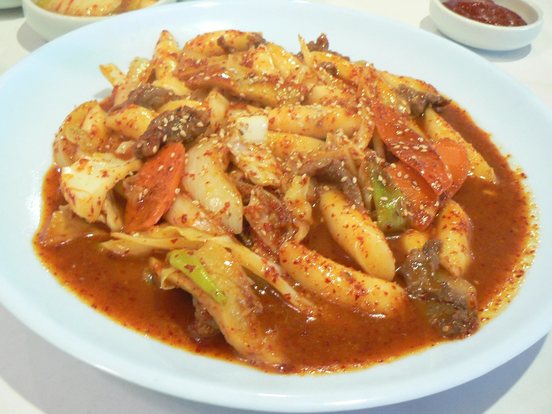 Gochujang : comprendre et utiliser la pâte de piment coréenne 9 Une assiette de gnocchis de riz coréens en sauce rouge, avec du bœuf, du chou et des flocons de piment en surface