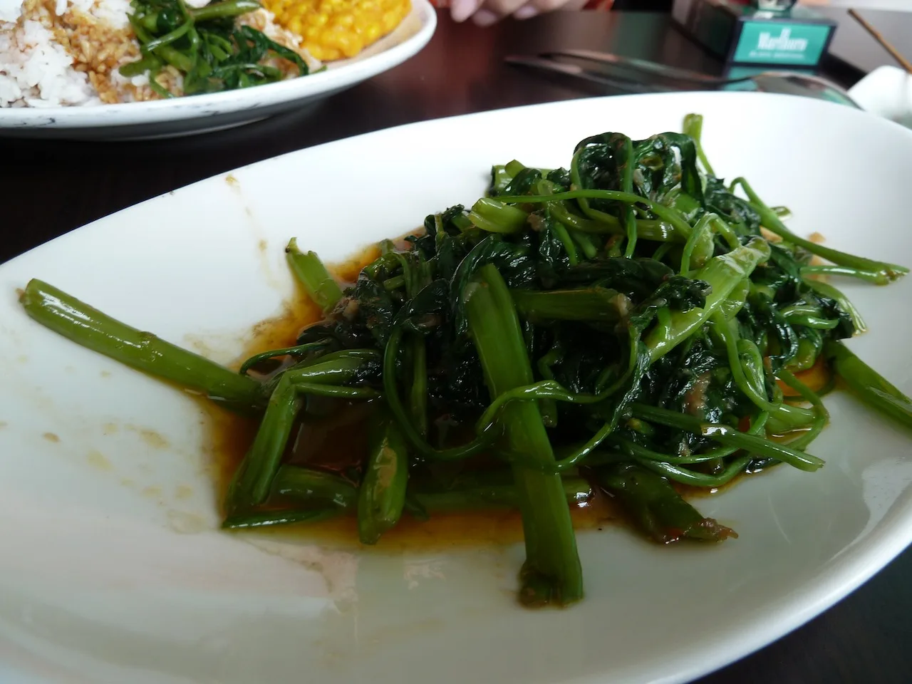 Sambal belacan : le condiment malaisien à la pâte de crevette 9 Une assiette de liseron d'eau sauté, aux longues tiges vert sombre, dans une sauce brun orangé
