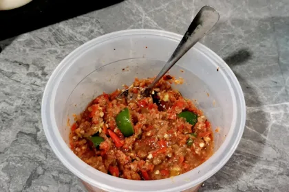 Un pot de sambal belacan maison, une pâte rouge grossièrement pilée avec des quartiers d'agrume vert, une cuillère plantée dedans
