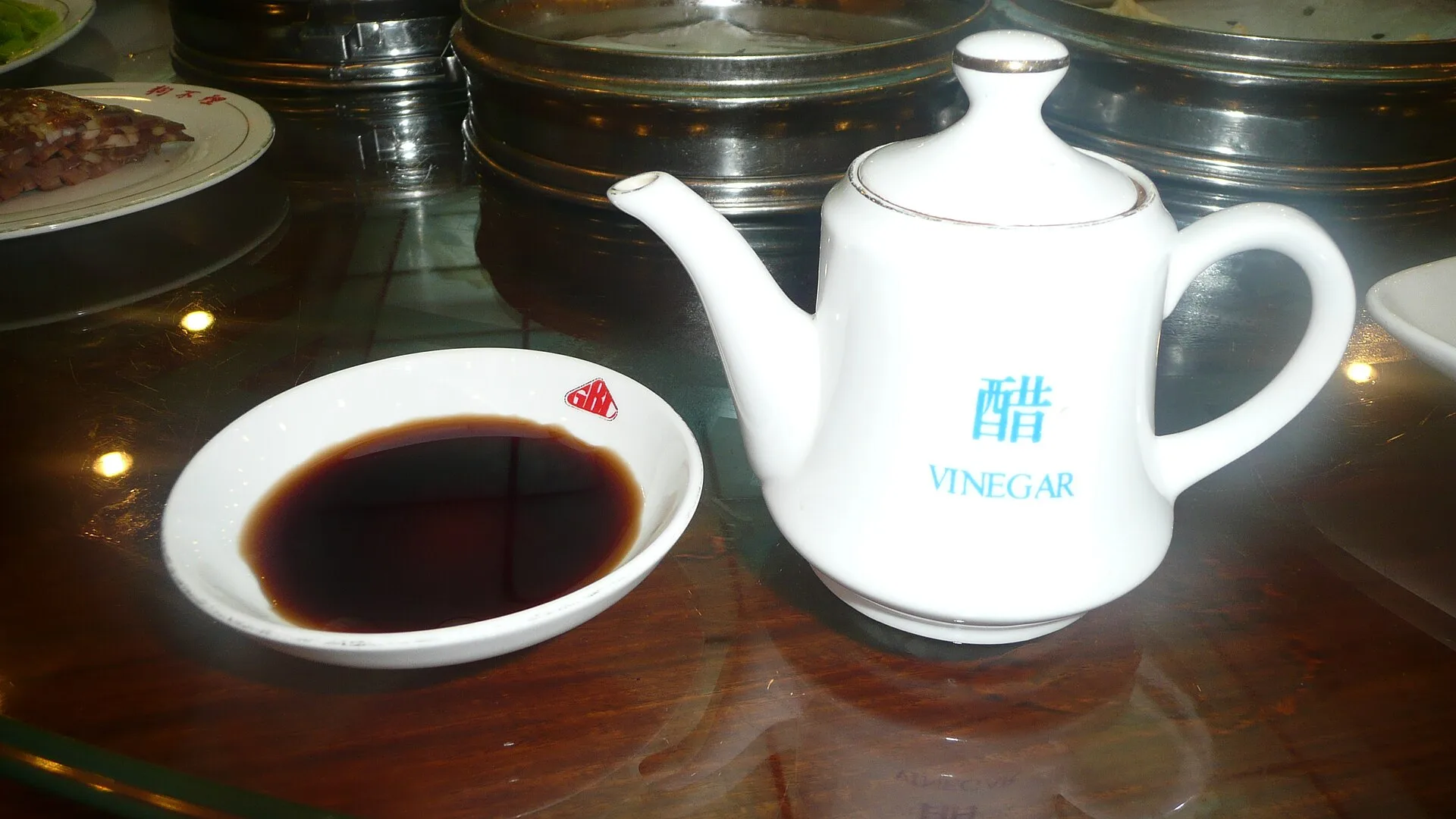 Une théière blanche marquée du caractère chinois du vinaigre, à côté d'une coupelle de vinaigre brun