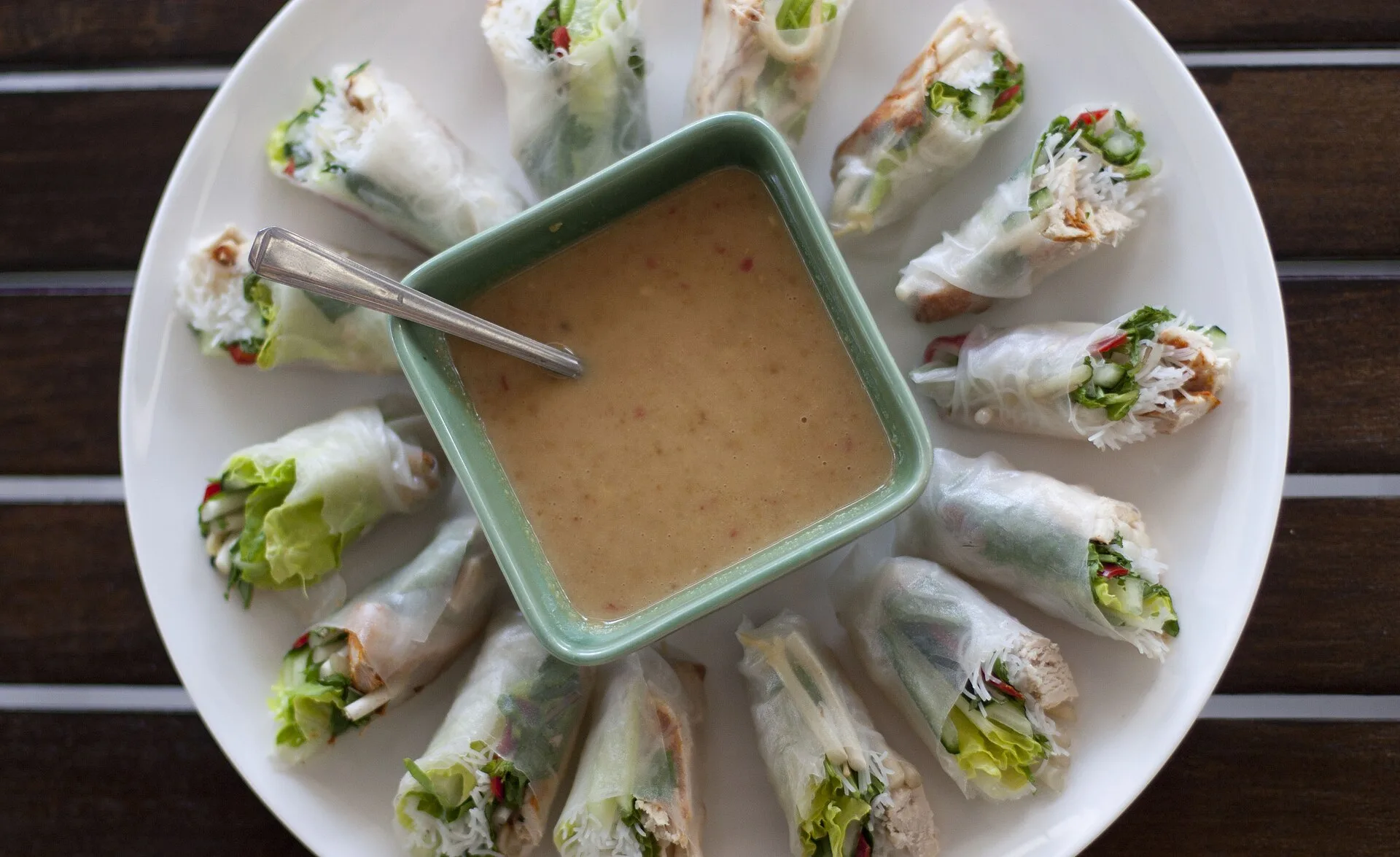 Sauce cacahuète pour rouleaux de printemps : la recette vietnamienne 8 Une assiette de rouleaux de riz disposés en cercle autour d'un bol carré de sauce cacahuète beige clair