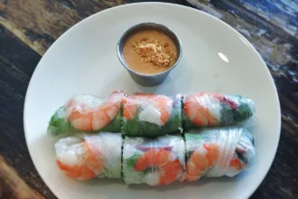 Deux rouleaux de printemps à la crevette en galette de riz translucide, avec une coupelle de sauce cacahuète parsemée de cacahuètes concassées