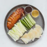 Des crêpes de canard laqué avec sauce hoisin, oignons et concombre, prêtes à être roulées