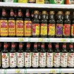Un rayon de supermarché chinois rempli de bouteilles de sauce soja de la même marque, étiquettes rouges et jaunes