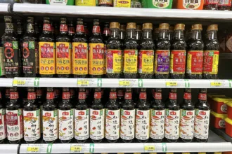 Un rayon de supermarché chinois rempli de bouteilles de sauce soja de la même marque, étiquettes rouges et jaunes