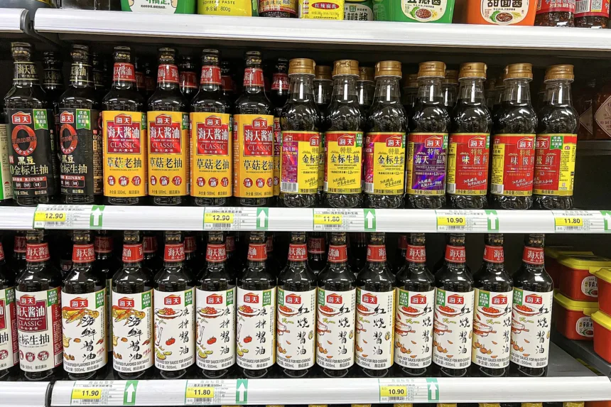 Un rayon de supermarché chinois rempli de bouteilles de sauce soja de la même marque, étiquettes rouges et jaunes