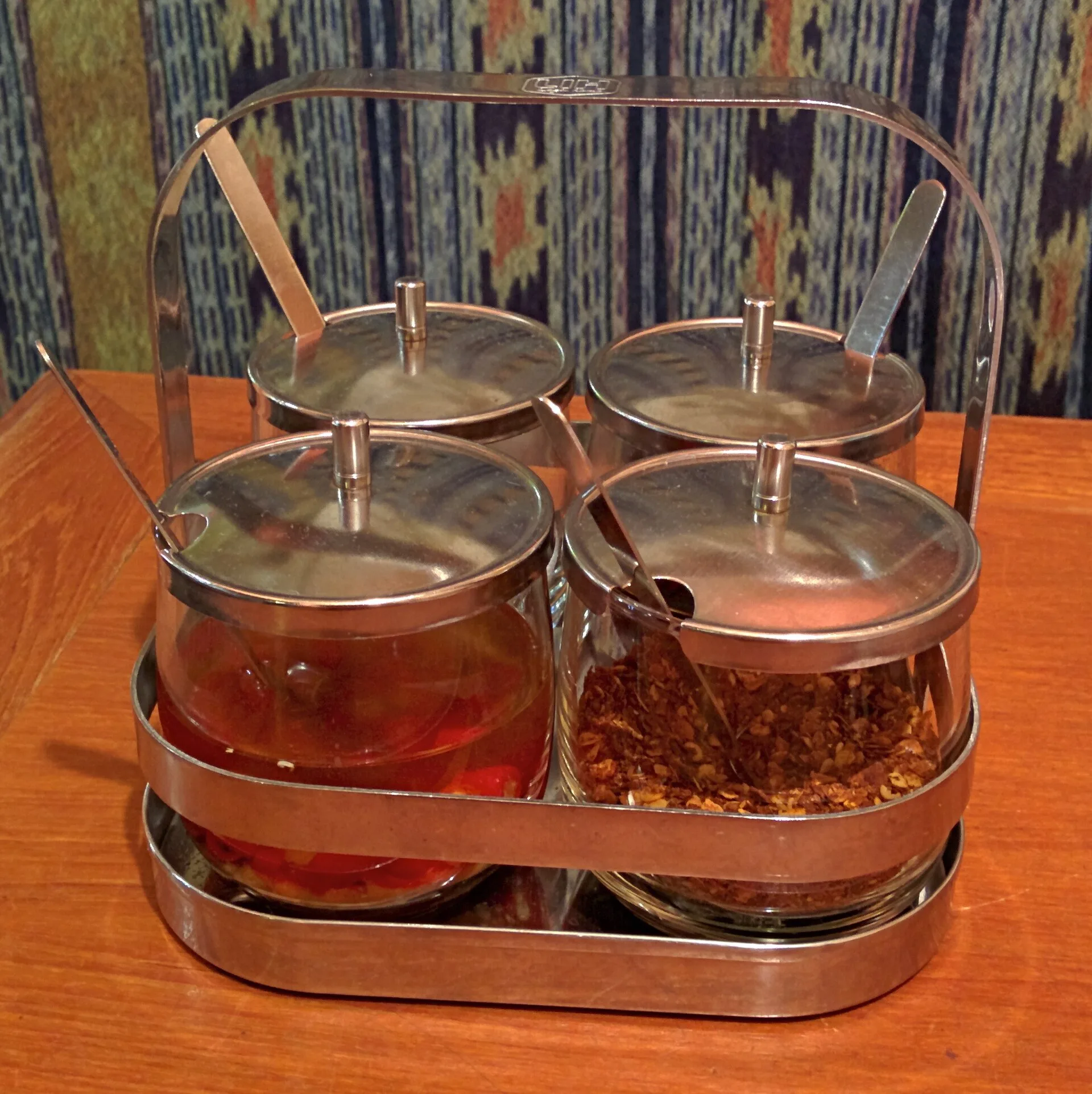 Sauces asiatiques : le guide pour savoir laquelle utiliser 9 Un présentoir métallique de quatre pots en verre sur une table en bois, l'un rempli de piments dans un liquide ambré, un autre de piment séché