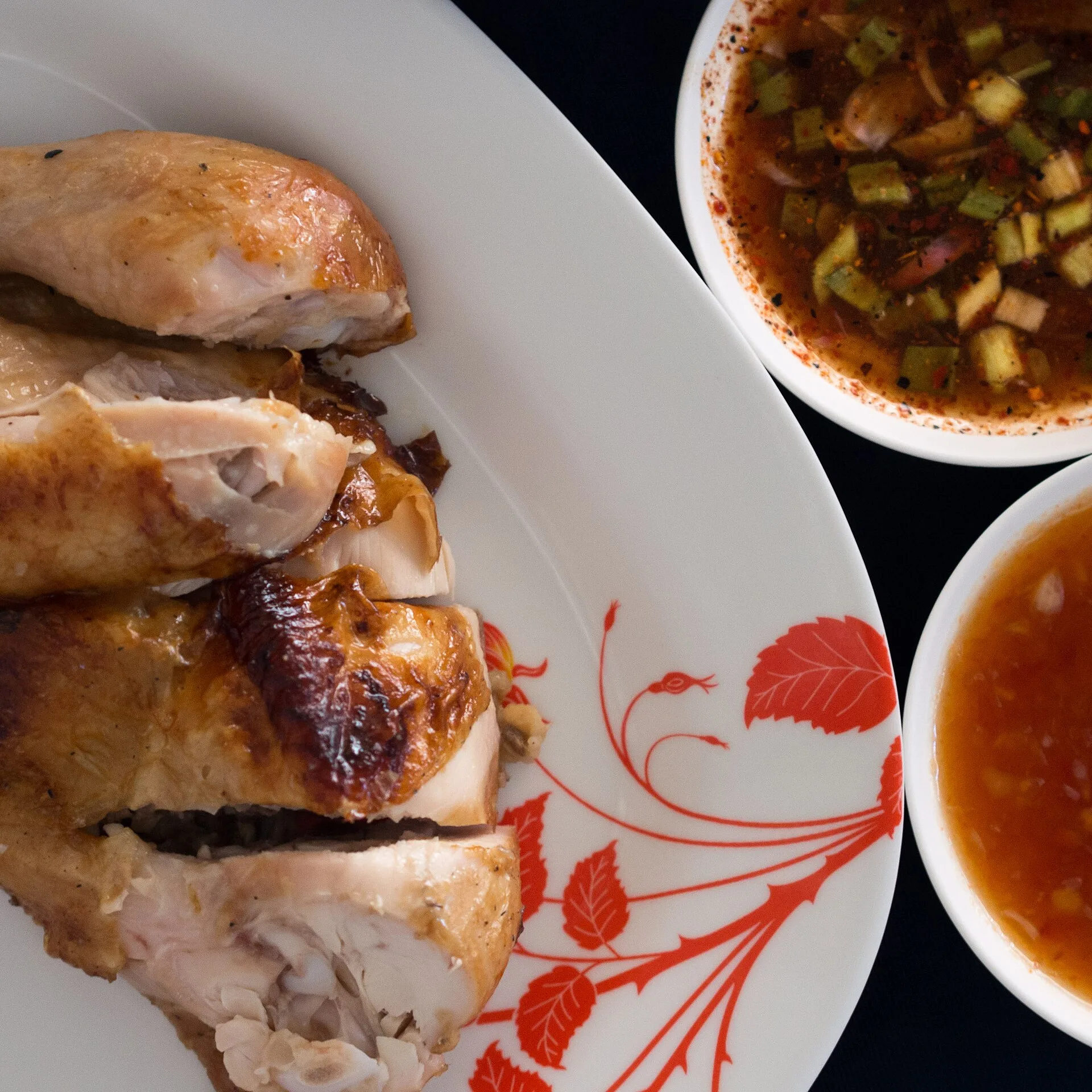 Un poulet grillé découpé servi avec deux bols de sauce, l'une brune et piquante, l'autre rouge et sucrée