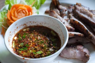 Un petit bol de sauce brun rougeâtre parsemée de flocons de piment, de grains de riz grillé et d'herbes hachées