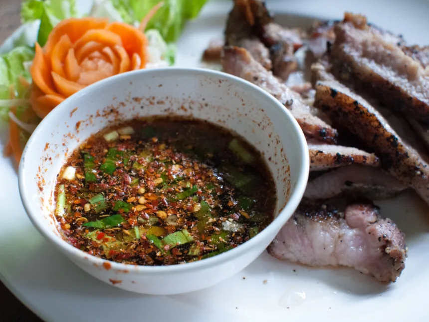 Un petit bol de sauce brun rougeâtre parsemée de flocons de piment, de grains de riz grillé et d'herbes hachées