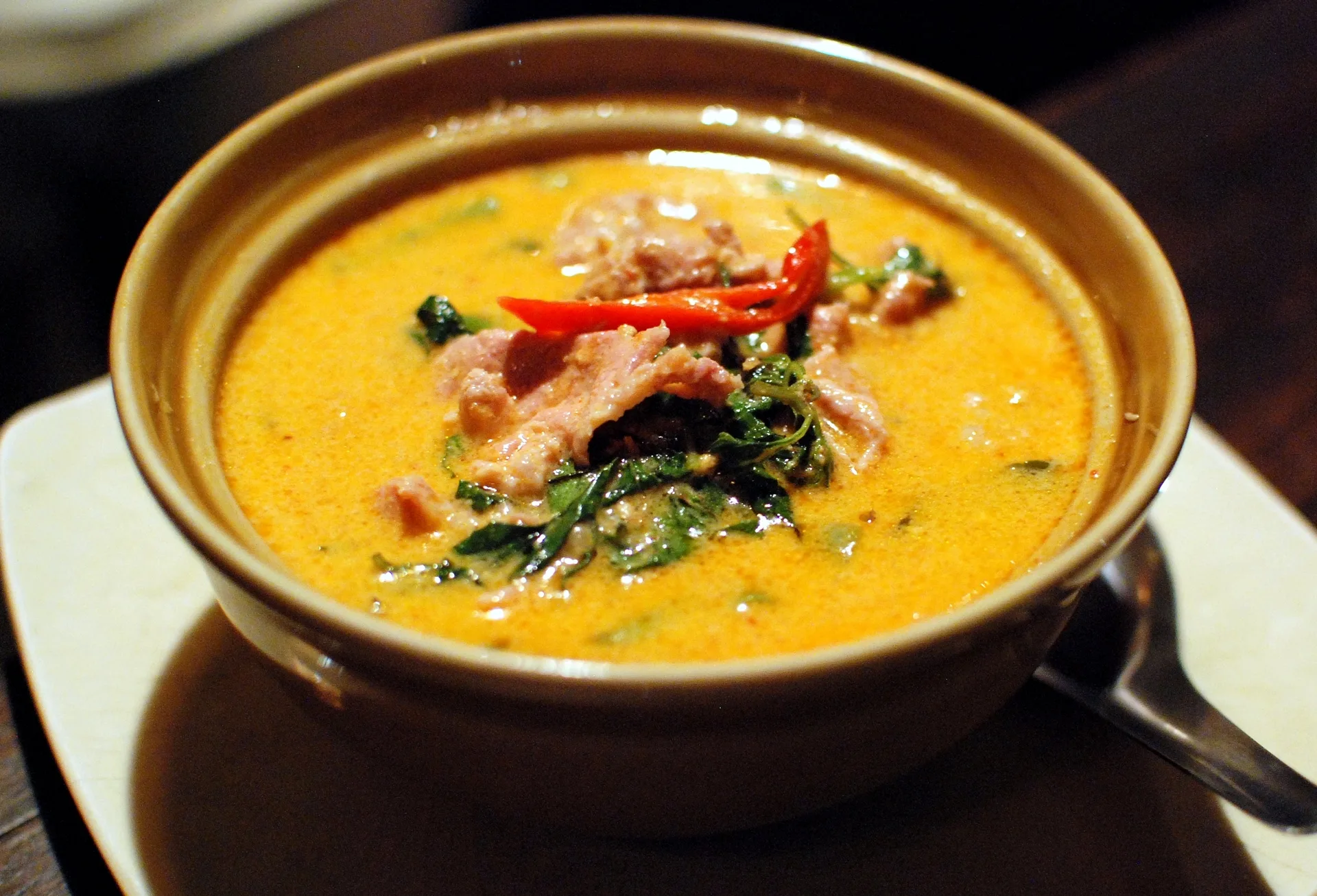 Un bol de curry rouge au porc, sauce orangée au lait de coco, garni de feuilles de basilic et d'un piment rouge en lanières
