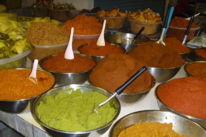 Un étal de marché couvert de bassines en inox remplies de pâtes de curry rouges, orange, brunes et vertes, chacune avec sa cuillère