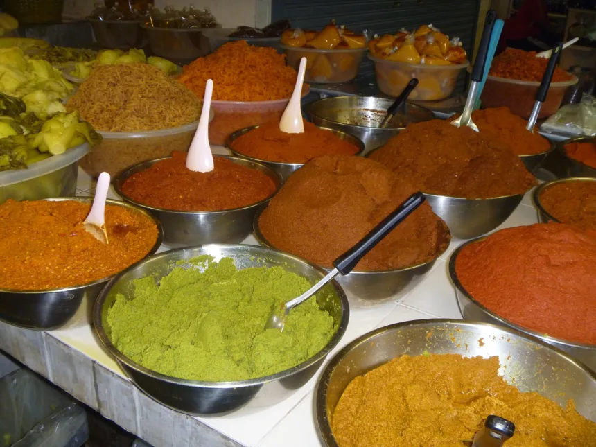 Un étal de marché couvert de bassines en inox remplies de pâtes de curry rouges, orange, brunes et vertes, chacune avec sa cuillère