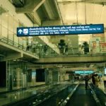 Intérieur de l'aéroport Suvarnabhumi à Bangkok, avec un tapis roulant et les panneaux des vols en correspondance